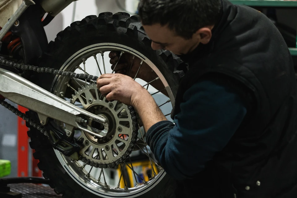 Mécanicien en combinaison de travail bleue inspectant le moteur d'une voiture au capot ouvert posée sur un pont élévateur hydraulique dans un atelier automobile professionnel, concentration sur la tâche de diagnostic.