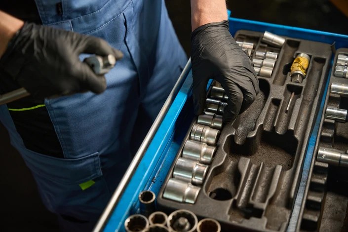 Mécanicien automobile souriant en combinaison bleue, bras croisés, posant sous un véhicule surélevé dans un garage professionnel
